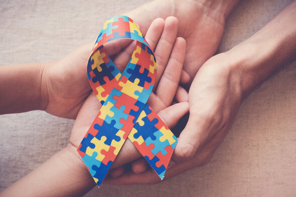 Mains d'un adulte et d'un enfant tenant le ruban en puzzle multicolore, symbole de la sensibilisation à l'autisme - Agrandir l'image, fenêtre modale