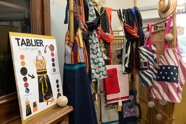 Espace boutique avec portant de textiles multicolores, sacs créateurs et panneau d'atelier tablier personnalisable