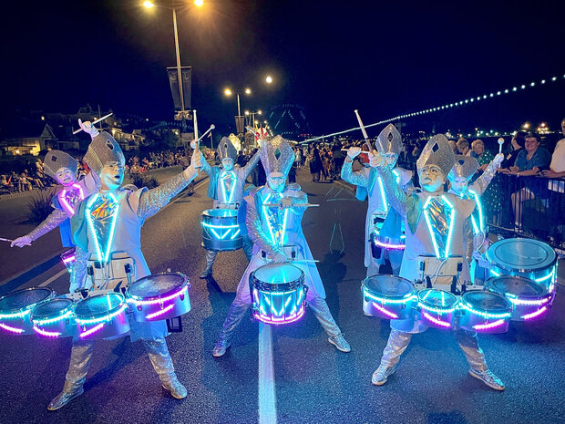 Percussionnistes en costumes argentés scintillants défilant de nuit, leurs tambours illuminés de LED bleues et cyan