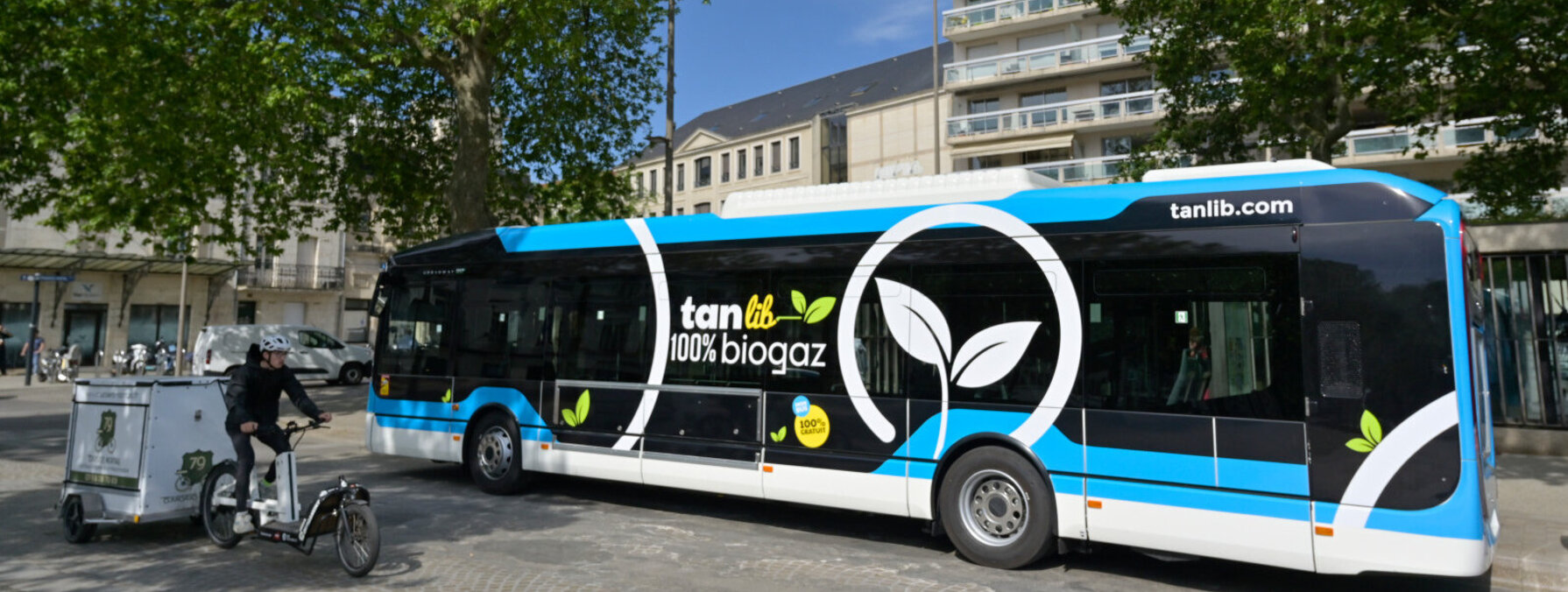 Bus articulé roulant au biogaz portant le marquage « TanLib 100 % biogaz », stationné sur la place de la Brèche