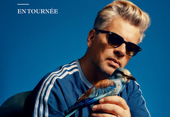Affiche de la tournée Benjamin Biolay, tenant un martin-pêcheur dans les mains, sur fond bleu intense - Agrandir l'image, fenêtre modale