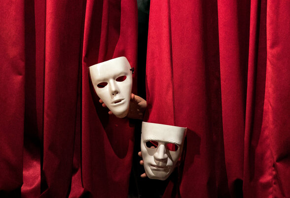 Trois masques de théâtre blancs surgissant entre les plis d'un rideau de scène rouge velours - Agrandir l'image, fenêtre modale