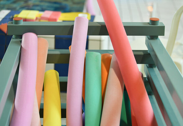 Frites de piscine multicolores rangées dans un rack métallique, accessoires d'aquagym au bord d'un bassin - Agrandir l'image, fenêtre modale