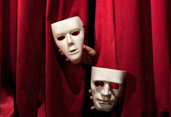 Des mains tendent trois masques blancs de théâtre à travers l'ouverture d'un rideau de scène rouge - Agrandir l'image, fenêtre modale