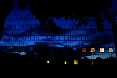Façade entièrement vitrée d'un bâtiment niortais reflétant le ciel nuageux au crépuscule, fenêtres éclairées de l'intérieur