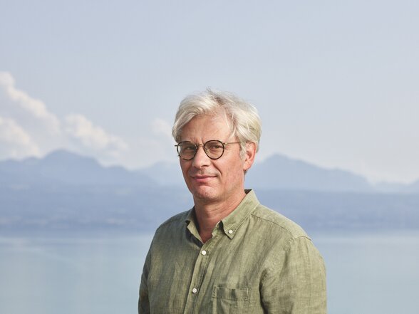 Roland Buti, écrivain suisse, posant devant un paysage lacustre et montagneux sous ciel brumeux - Agrandir l'image, fenêtre modale