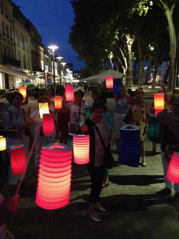 Participants tenant des lampions colorés allumés lors d'une sortie nocturne dans une rue arborée - Agrandir l'image, fenêtre modale