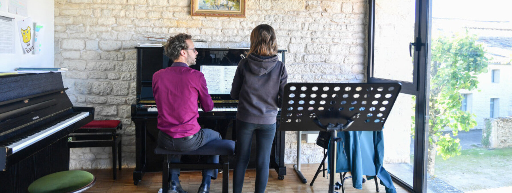 Cours de piano à l'antenne de Chauray : un professeur au clavier accompagne un élève debout face à la partition