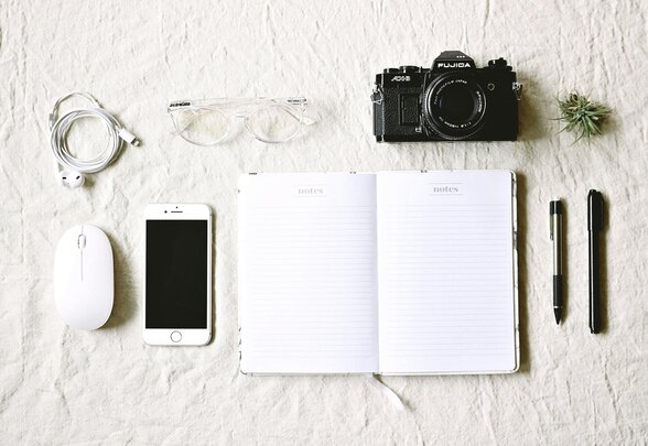 Carnet ouvert, appareil photo argentique Fujifilm, smartphone, souris et stylos posés à plat sur fond blanc - Agrandir l'image, fenêtre modale