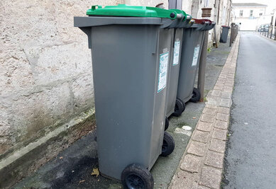 Rangée de conteneurs de collecte gris à couvercle vert alignés sur un trottoir en centre-ville