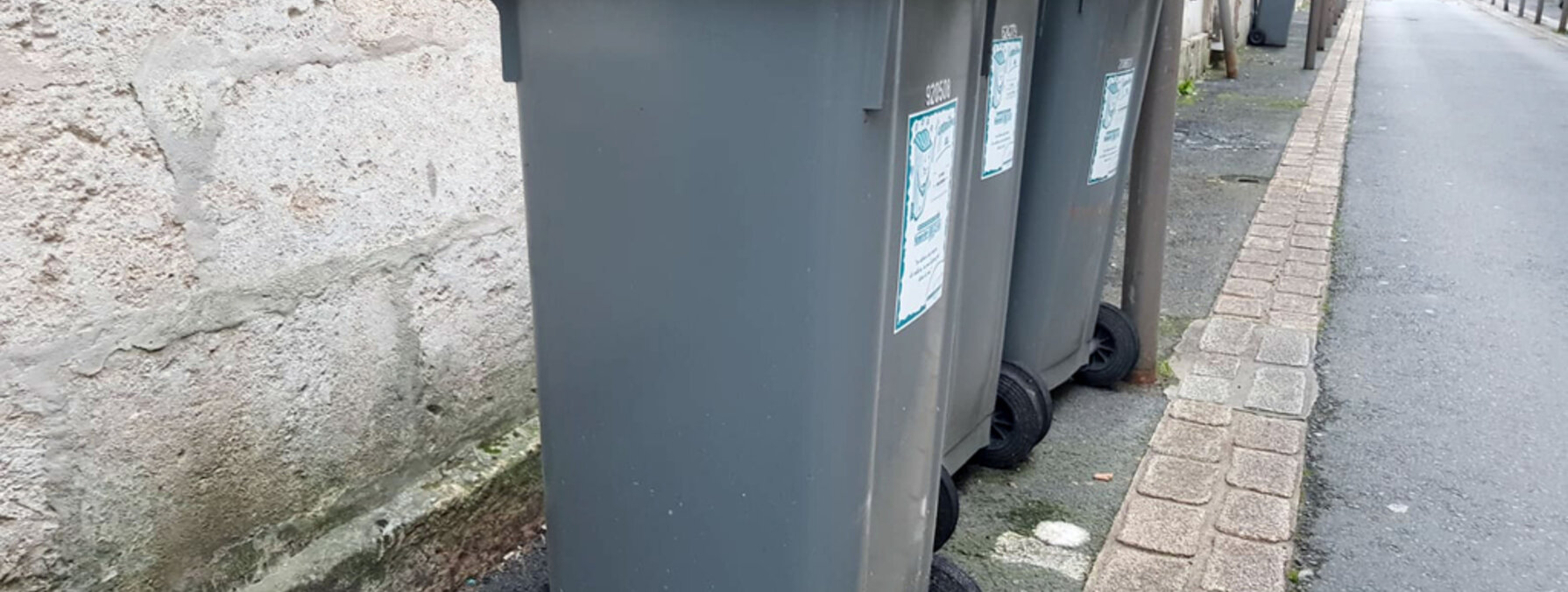 Rangée de conteneurs de collecte gris à couvercle vert alignés sur un trottoir en centre-ville