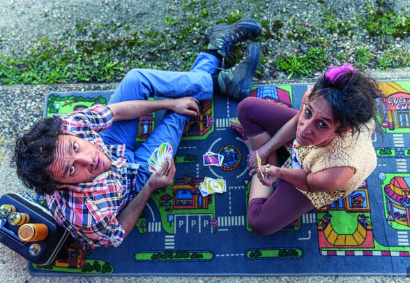 Deux artistes de cirque en tenue colorée jouent aux cartes sur un tapis enfant, photographiés en plongée - Agrandir l'image, fenêtre modale