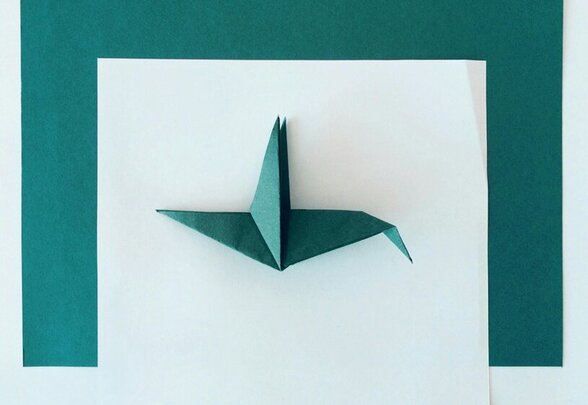 Grue en papier vert foncé (tsuru), figure symbolique façonnée à partir d'une simple feuille, posée sur fond blanc - Agrandir l'image, fenêtre modale