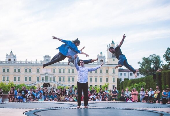 Deux artistes bondissent haut dans les airs au-dessus du plateau circulaire, devant une foule nombreuse et un palais en plein air - Agrandir l'image, fenêtre modale