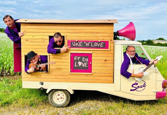 Les quatre musiciens du S.O.U.K en costume violet, autour d'un triporteur à cabane en bois orné d'un mégaphone rose, ukulélés à la main - Agrandir l'image, fenêtre modale