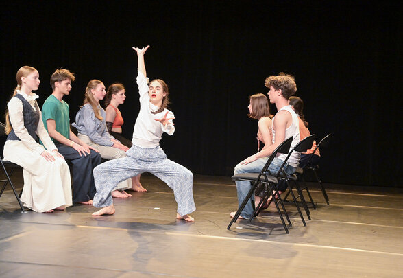 Performance de danse sur scène : une élève exécute un mouvement bras levé face aux autres élèves assis sur des chaises - Agrandir l'image, fenêtre modale