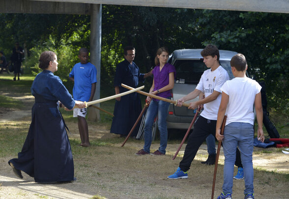 Démonstration de kendo en plein air : un pratiquant en tenue traditionnelle face à deux jeunes avec des bokken - Agrandir l'image, fenêtre modale