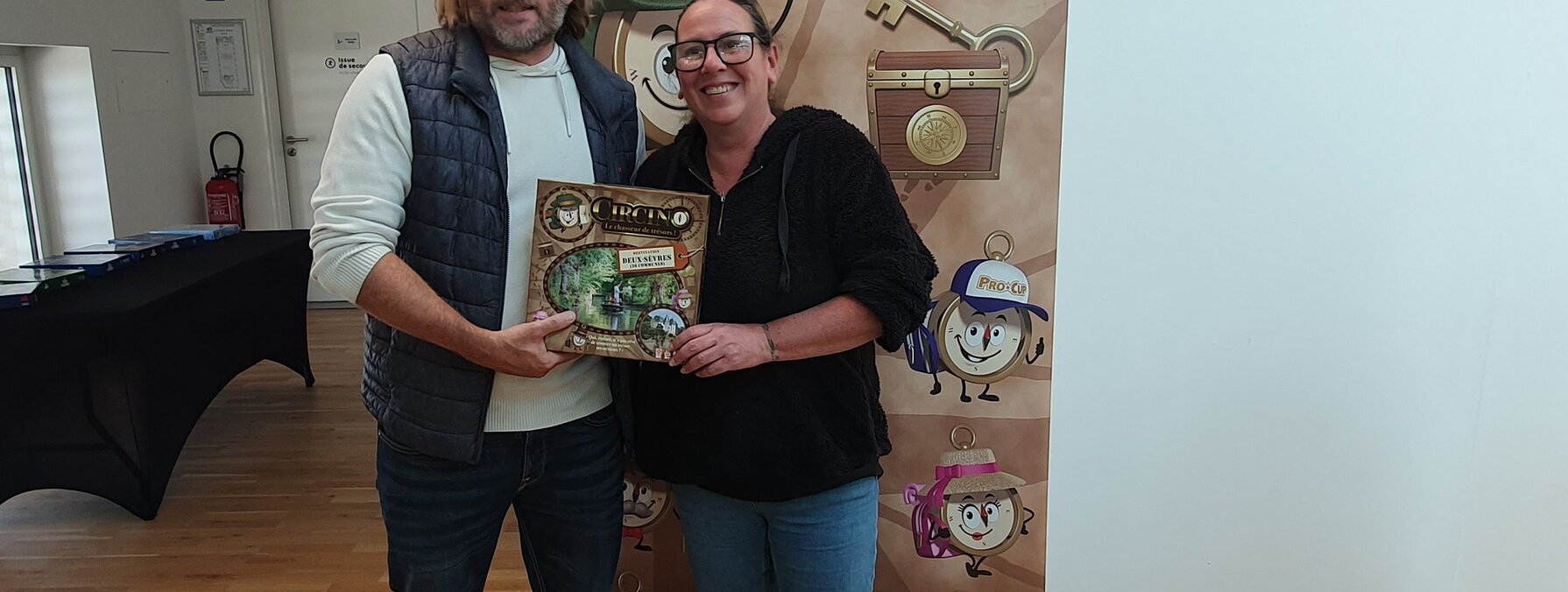 Deux personnes présentant la boîte de Circino 79 devant le kakémono du jeu « Le chasseur de trésors »