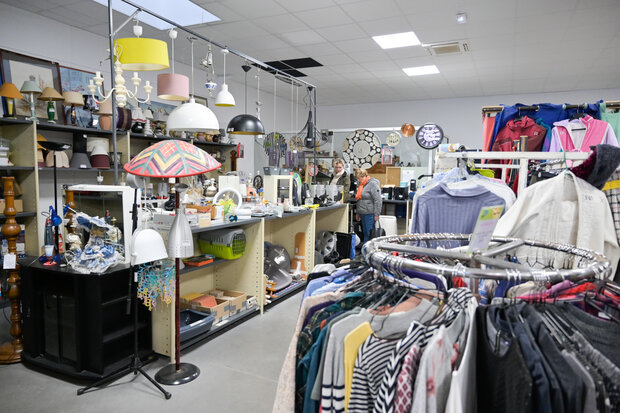 Intérieur d'une ressourcerie avec portants de vêtements, luminaires suspendus et étagères garnies d'objets de seconde main