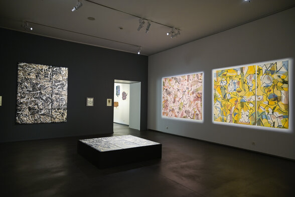 Salle du musée avec de grandes toiles abstraites en noir-blanc et couleurs vives, et une œuvre posée à plat sur un socle central - Agrandir l'image, fenêtre modale
