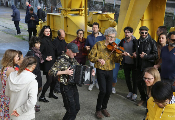 Un accordéoniste et un violoniste animent une ronde de participants réunis en plein air autour d'eux - Agrandir l'image, fenêtre modale