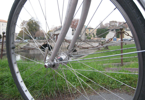 Roue de vélo en gros plan avec un bord de rivière et des bâtiments en arrière-plan - Agrandir l'image, fenêtre modale