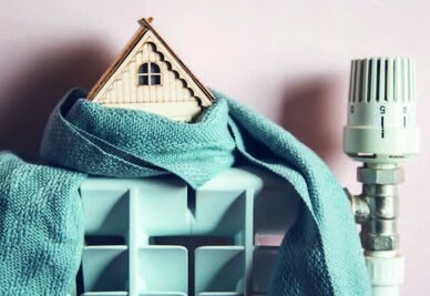 Maquette de maison enveloppée dans un tissu posée sur un radiateur avec tête thermostatique