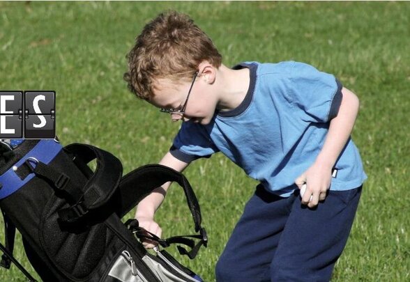 Enfant penché sur un sac de golf posé sur le gazon d'un parcours, prêt à choisir un club - Agrandir l'image, fenêtre modale
