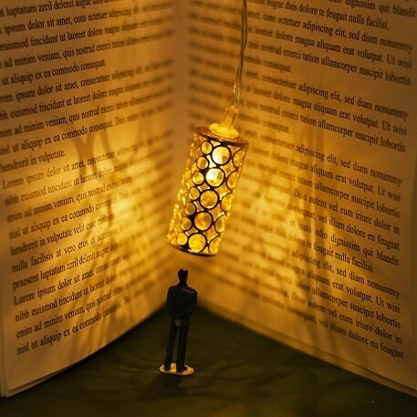 Personnage miniature debout dans un livre ouvert géant, éclairé par une lanterne suspendue, symbole de l'immersion dans la lecture - Agrandir l'image, fenêtre modale