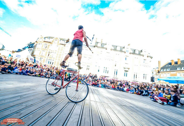 Artiste de cirque debout sur un vélo rouge jonglant devant une grande foule en plein air - Agrandir l'image, fenêtre modale