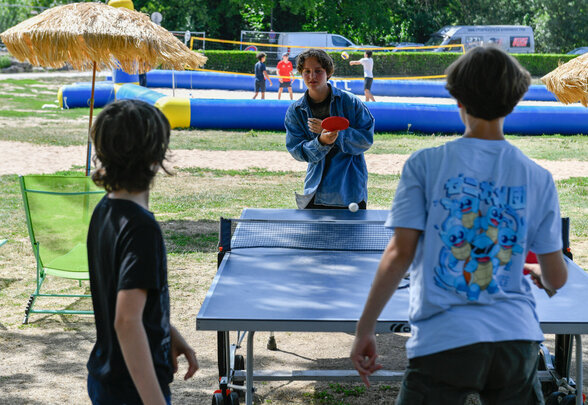 Jeunes jouant au tennis de table en plein air lors de Niort Plage, avec un terrain de beach-volley gonflable en arrière-plan - Agrandir l'image, fenêtre modale