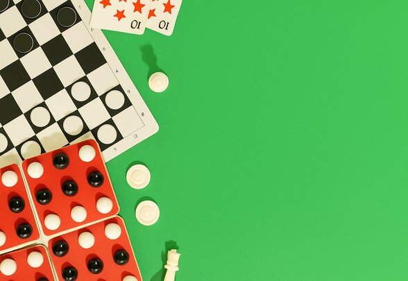 Plateau de jeu de dames, dominos rouges, cartes à jouer et pièces d'échecs posés sur fond vert - Agrandir l'image, fenêtre modale