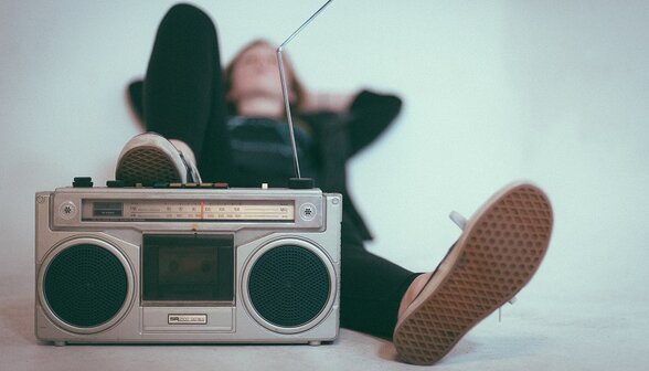 Personne allongée sur le sol en position détendue, un radio-cassette vintage posé devant elle - Agrandir l'image, fenêtre modale