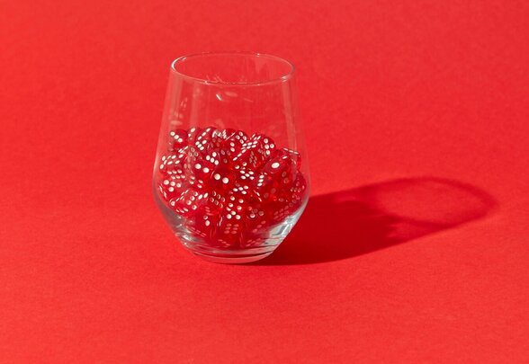 Verre transparent rempli de nombreux dés rouges à points blancs, posé sur un fond rouge vif - Agrandir l'image, fenêtre modale