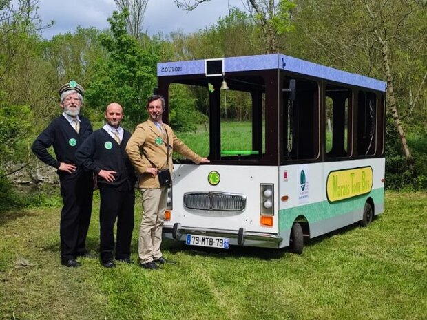 Trois membres de l'équipe Caus'toujours en tenue officielle posant devant le bus pédestre affichant la destination Coulon