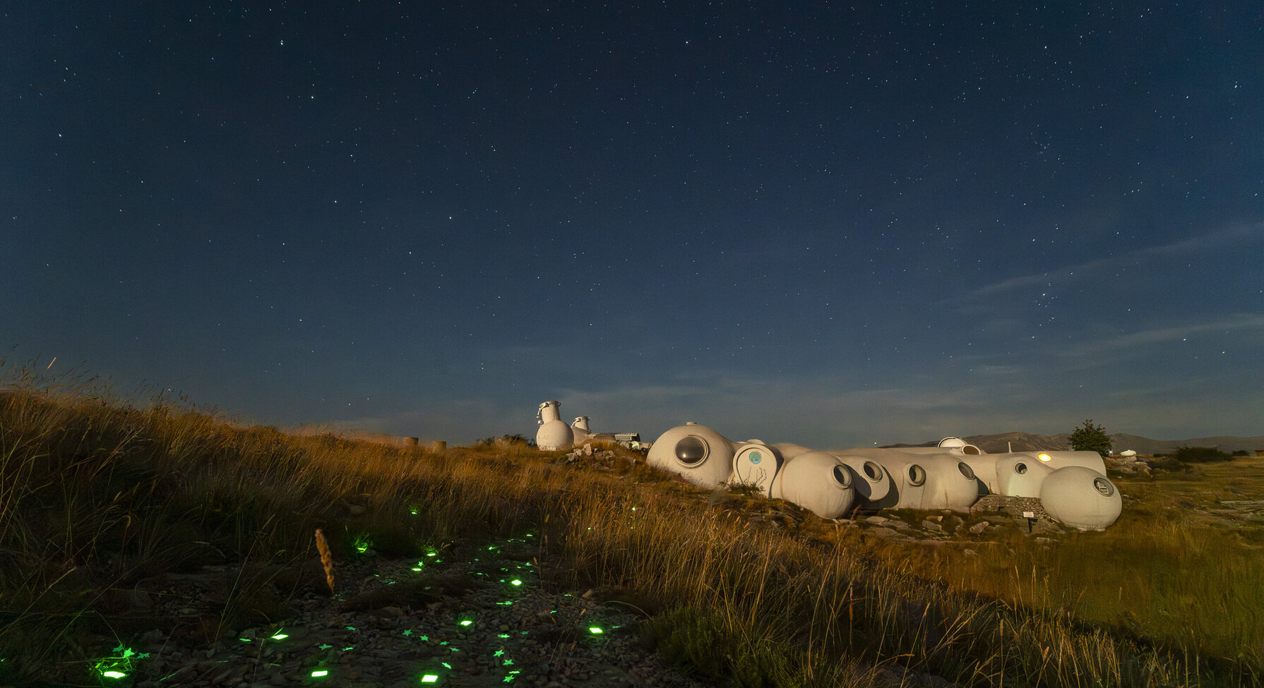 Structures en forme de dômes blancs illuminées la nuit sous un ciel étoilé, avec des lumières vertes en forme d'étoiles au sol