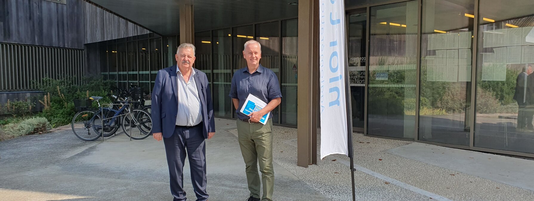 Représentants de Niort Agglo et tanlib posant devant l'entrée du Siège de Niort Agglo, l'un tenant un document de présentation