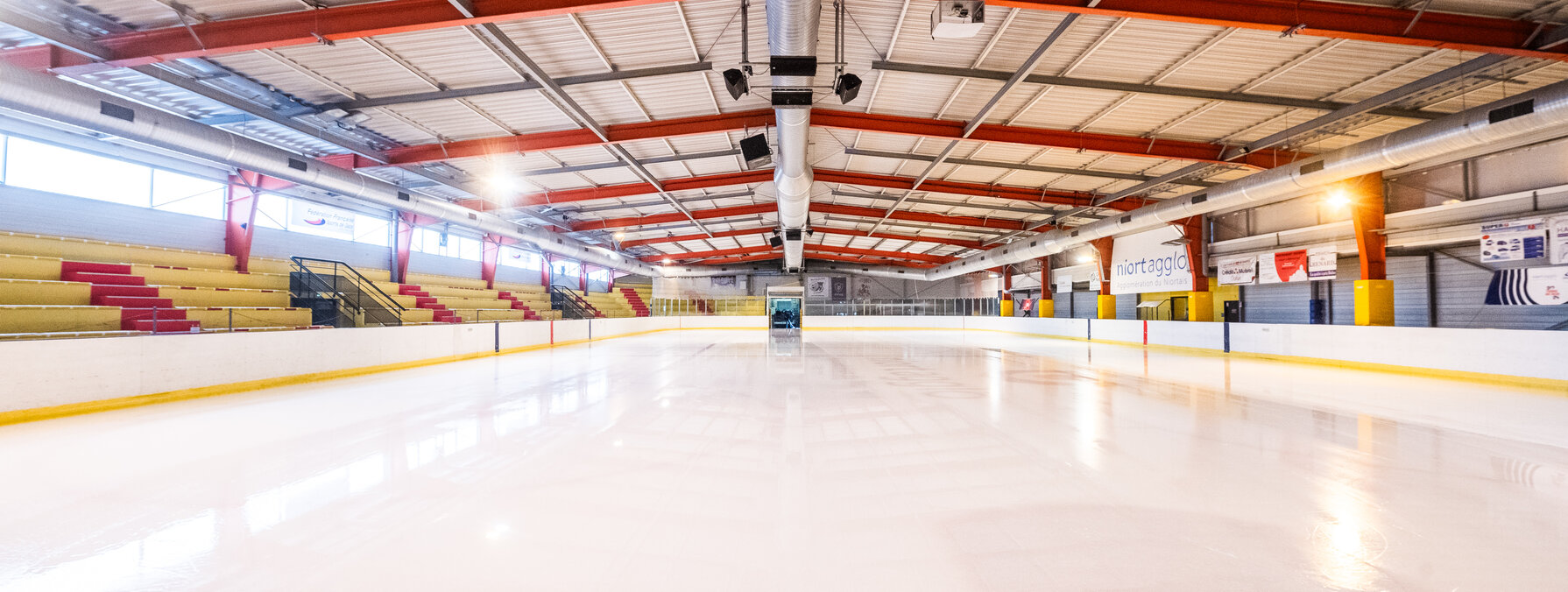 Piste de glace lisse et brillante fraîchement surfacée, tribunes vides et charpente métallique rouge de la patinoire en arrière-plan