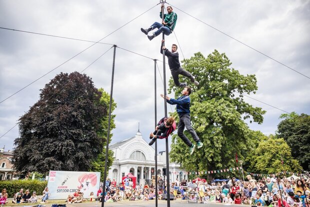 Quatre acrobates enchaînés en cascade sur un même mât en hauteur, sous les yeux d'une foule nombreuse