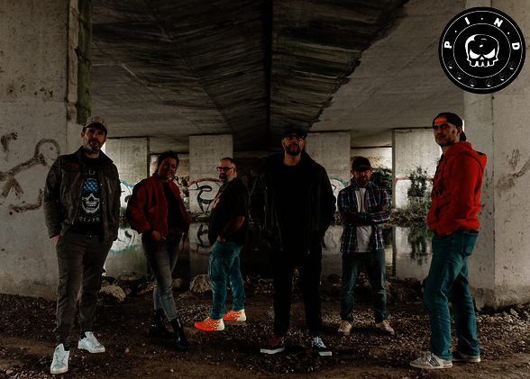 Les six membres du groupe P.I.N.D posent sous un pont couvert de graffitis, logo du groupe visible en haut à droite. - Agrandir l'image, fenêtre modale