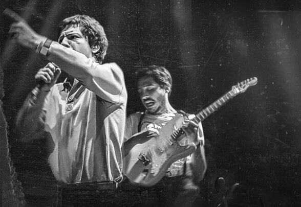 Performance scénique en noir et blanc : chanteur micro en main et guitariste électrique en pleine action - Agrandir l'image, fenêtre modale