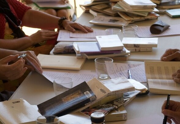 Participants réunis autour d'une table couverte de livres et cahiers, stylos en main, en pleine session d'écriture collective. - Agrandir l'image, fenêtre modale