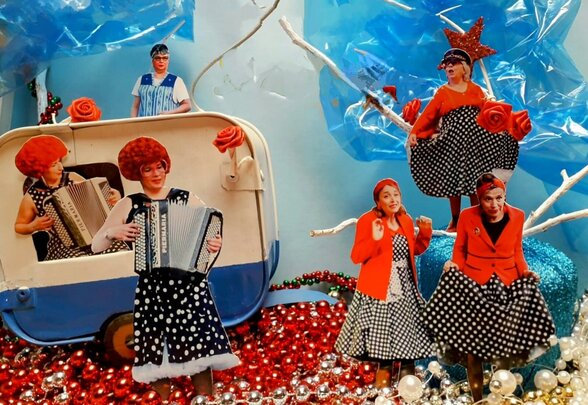 Scène artistique colorée : cinq performeuses en robes à pois et vestes rouges, dont une accordéoniste, dans un décor festif bleu et rouge - Agrandir l'image, fenêtre modale