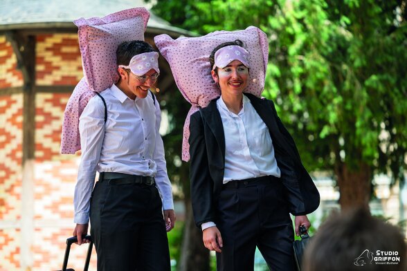 Deux artistes en costume noir et blanc, grands oreillers roses sur la tête et masques de nuit, souriants lors d'une représentation en plein air - Agrandir l'image, fenêtre modale