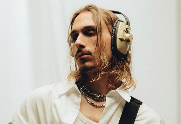 Musicien aux longs cheveux blonds tenant une guitare électrique, casque audio sur la tête, regard concentré - Agrandir l'image, fenêtre modale