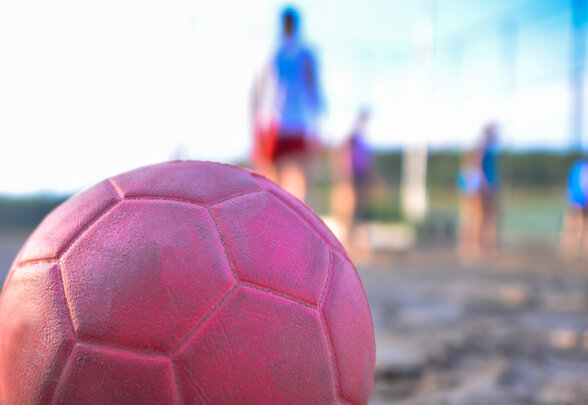 Ballon rose de beach handball posé sur le sable, joueurs floutés en arrière-plan sur un terrain extérieur - Agrandir l'image, fenêtre modale