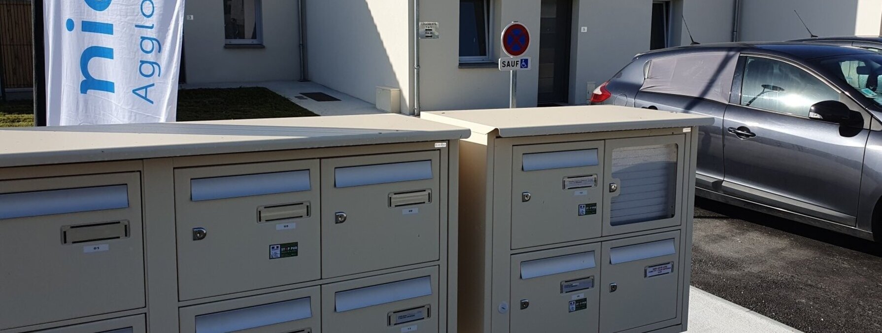 Boîtes aux lettres collectives devant des maisons individuelles neuves, avec la bannière Niort Agglomération