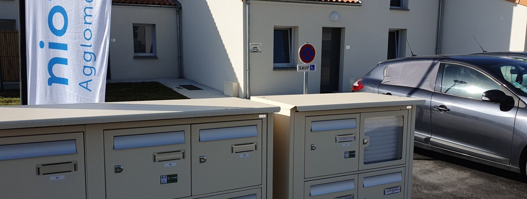 Boîtes aux lettres collectives devant des maisons individuelles neuves, avec la bannière Niort Agglomération