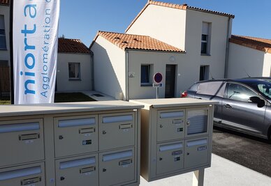 Boîtes aux lettres collectives devant des maisons individuelles neuves, avec la bannière Niort Agglomération