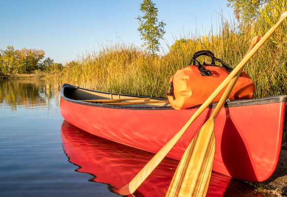 Canoë rouge avec pagaies en bois et sac étanche posé sur la rive d'une rivière calme aux reflets automnaux - Agrandir l'image, fenêtre modale